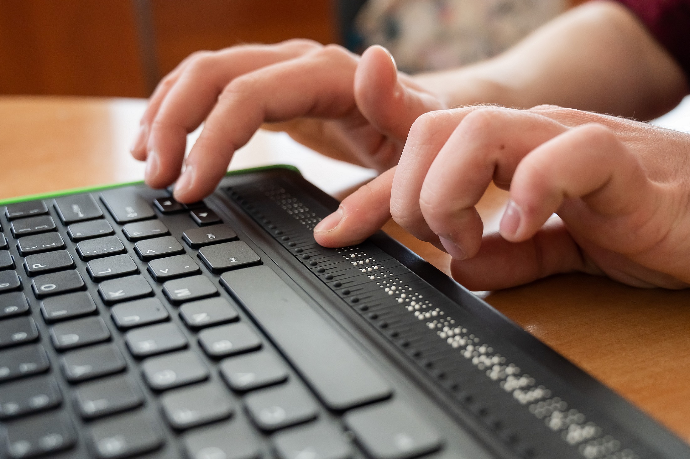 Image of a close up of two hands typing on a black braille keyboard.